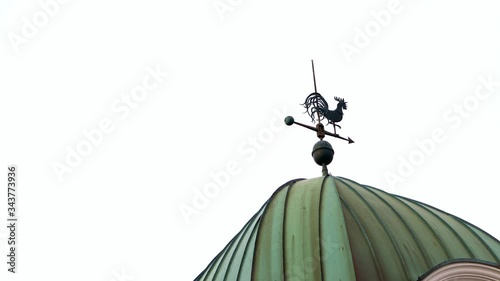Wrought iron vintage retro weather vane instrument made to resemble arrow with proud rooster on top showing wind direction mounted on top of old barn metal roof on clear sky background