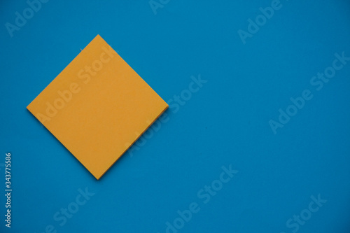 Bright orange posted note on bright blue flat lay background for education or business organization and reminder concepts.
