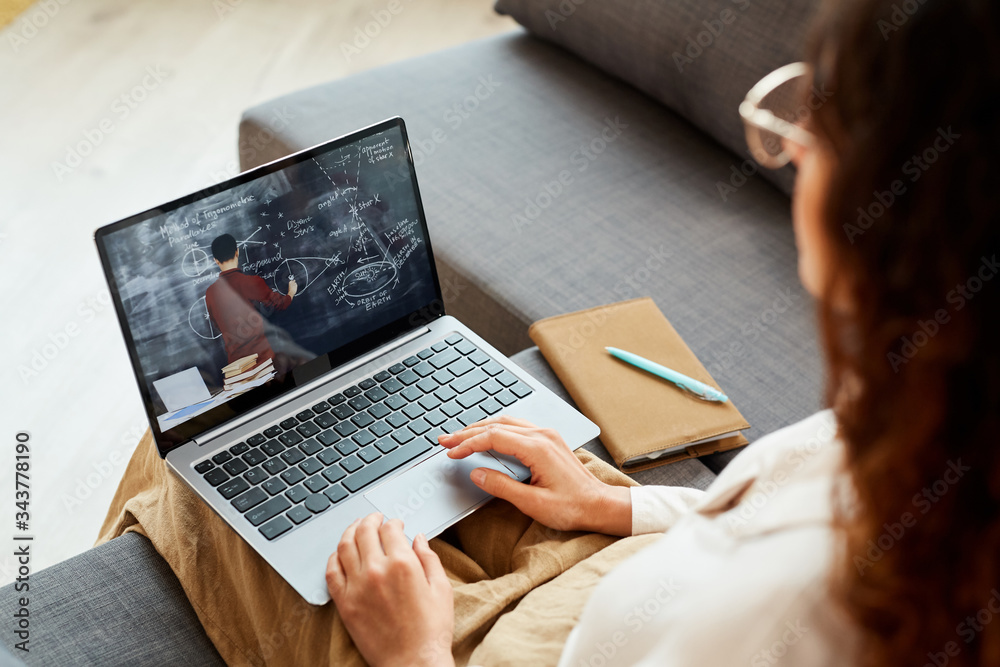 Unrecognizable woman sitting on sofa at home watching online conference video, horizontal high angle shot