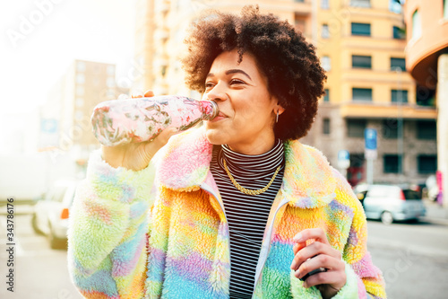 Young beautiful multiethnic woman outdoors drinking from reusable bottle photo