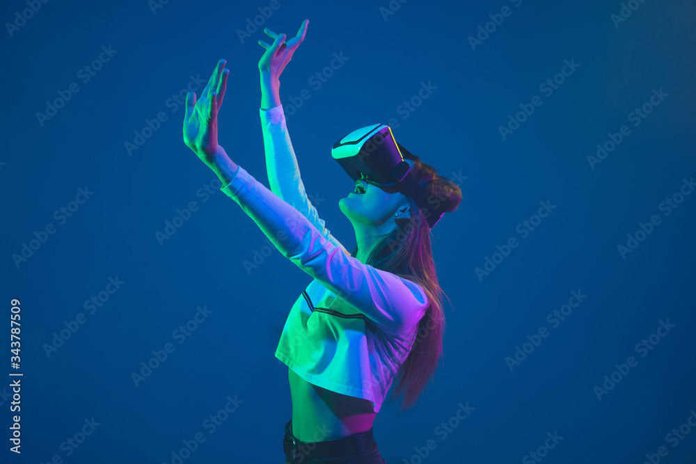 Playing in action. Caucasian young woman's portrait isolated on blue studio background in neon light. Beautiful female model. Concept of human emotions, facial expression, sales, ad, youth culture.