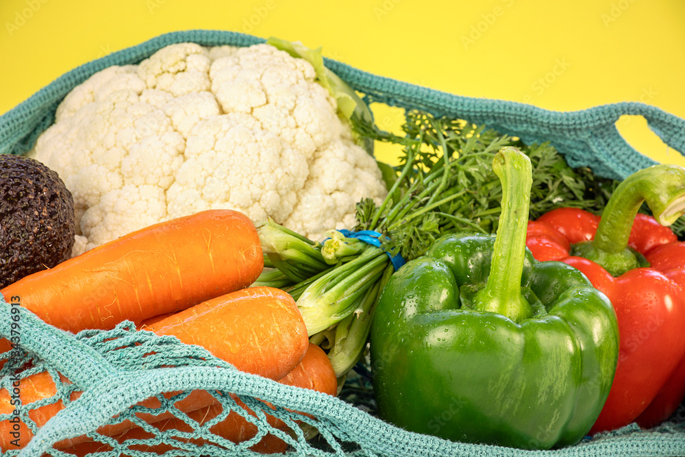 Close up of fresh vegetables in mesh bag, on yellow background, colorful composition. Various vegetables arrangement, healthy eating concept. Close up of fresh vegetables in mesh bag, on yellow background, colorful composition. Various vegetables arrangement, healthy eating concept.