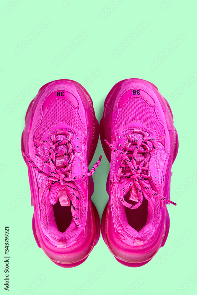 Pair of new trendy fuchsia sneakers isolated on a light green background with shadow. Top view.