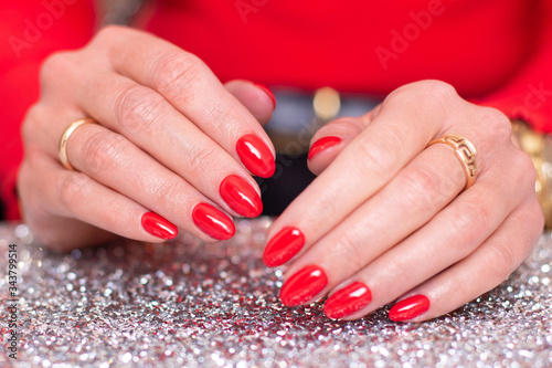 Close up view of female hands with beautiful luxury red manicure  nails with red gel polish on sparkling background