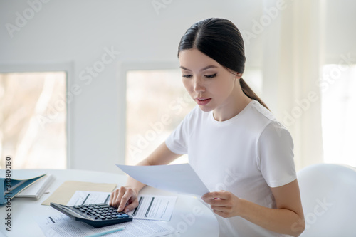 Brunette female sitting at her desk  holding papers  pressing calculator