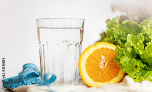 salade leaf. orange, cup of water and measuring blue tape on white background , healthy lifestyle and drinking water concept