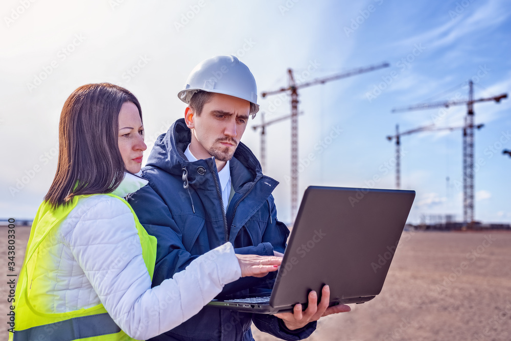 A builder and a real estate agent look into a laptop against the background of a building under construction. A builder and a real estate agent look into a laptop against the background of a building under construction.