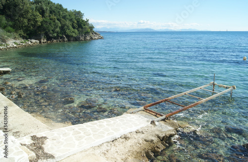 An old metal jetty on the coast at the beautiful Greek island of Corfu.  Wooded cliffs by the waters edge at the quiet, family, resort of Nissaki on the islands east coast. photo