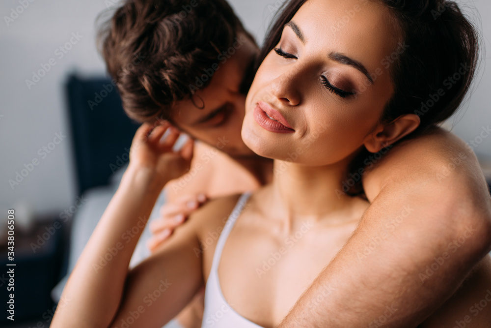 Selective focus of man hugging and kissing attractive girl with closed eyes in bedroom