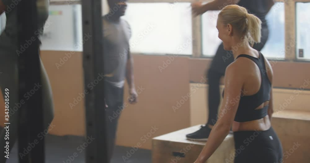 Smiling group of fit young people doing box jumps
during a workout together at the gym
