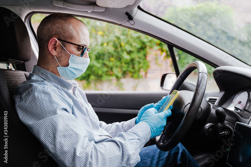 man using mobile phone in a car wearing protective mask and gloves during pandemic coronacirus covid-19