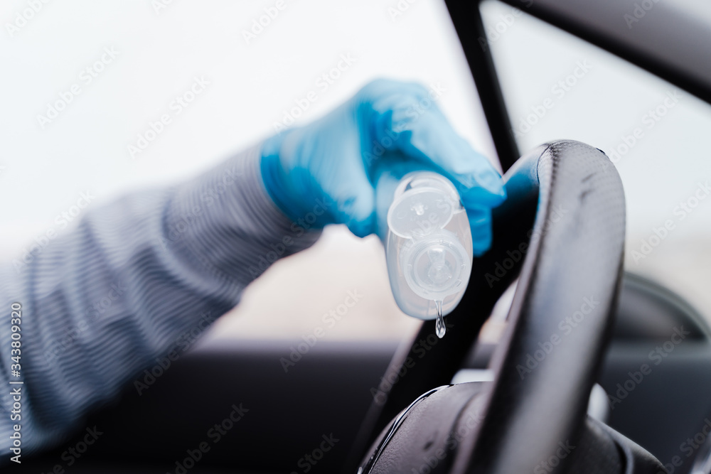 unrecognizable man in a car using alcohol gel to disinfect steering wheel during pandemic coronavirus covid-19