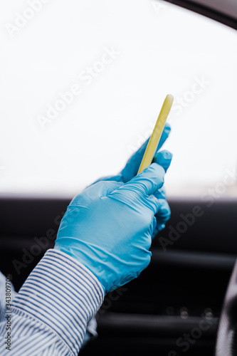 man using mobile phone in a car wearing protective mask and gloves during pandemic coronacirus covid-19