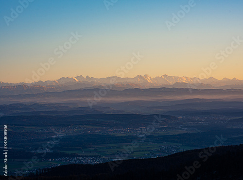 Swiss horizon during corona-virus COVID-19 pandemic with great visibility over a Central Valley or Flatland on Alps mountains from Jura mountains in canton Basel-Land at colorful sunset.