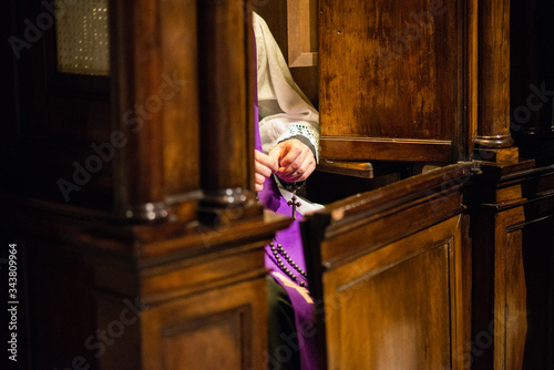 Photo priest in the confessional recites the rosary awaiting penitent