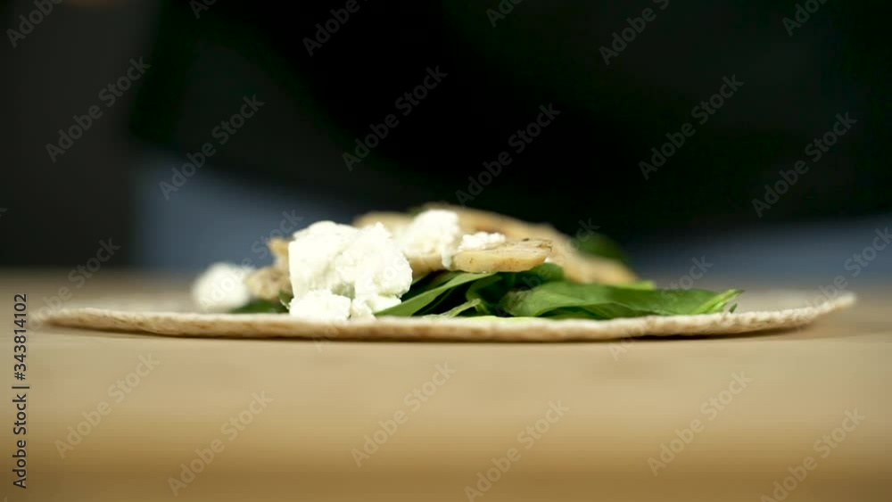 Las manos de una chica joven ponen queso feta sobre un wrap de espinacas.