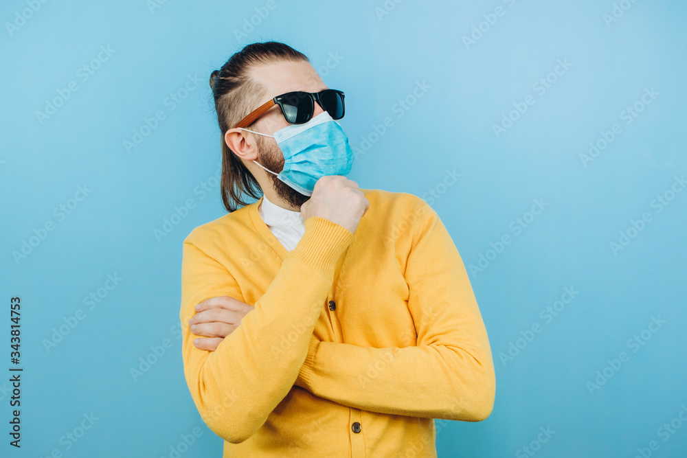 a man with glasses and a medical mask on a blue background. An emotional and positive guy on self-isolation. Coronavirus. Studio shooting. Pandemic COVID 19. a man with glasses and a medical mask on a blue background. An emotional and positive guy on self-isolation. Coronavirus. Studio shooting. Pandemic COVID 19.