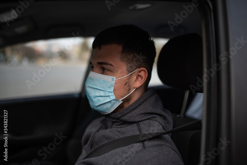a man driving a car puts on a medical mask during an epidemic, a taxi driver in a mask, protection from the virus. Driver in black car. coronavirus, disease, infection, quarantine, covid-19 © Evghenii Blanaru