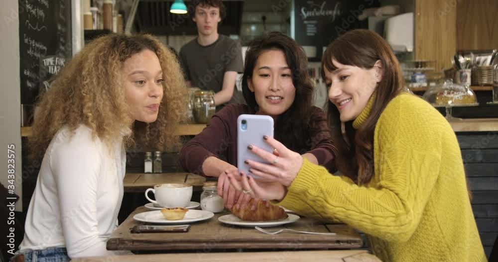 A Woman Shows Her Friends Something Funny On Phone In Cafe A Woman Shows Her Friends Something Funny On Phone In Cafe