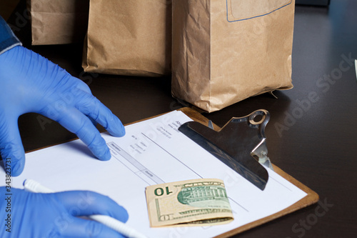 Paper bags with food, delivery form and dollar bills. A man in rubber gloves takes the order. Home delivery during an epidemic.