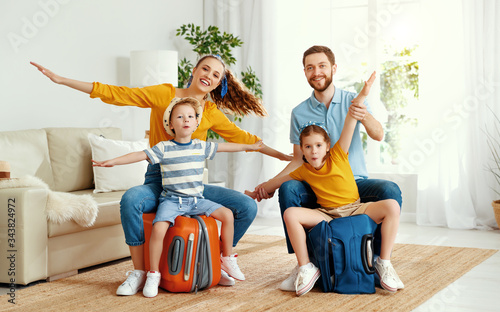 Happy parents and kids on suitcases in living room.