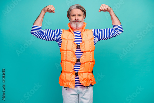 Photo of attractive aged guy show two biceps arms strong mariner sea ocean ship trip sportsman wear striped sailor shirt shorts orange vest isolated teal color background photo