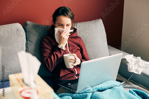 Obraz na płótnie sick girl works remotely at home with cup of tea and tissues on the bed w salonie