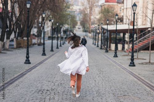 girl or woman in a white medical coat runs away along the street. doctor, nurse runs around the city. coronavirus, disease, infection, quarantine, covid-19