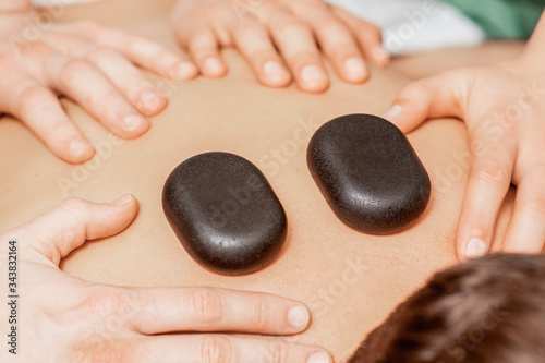 Close up massage therapists hands doing back massage with hot stones on back of man in spa.