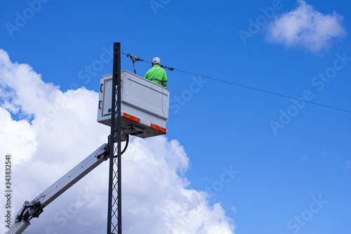 Lineworker working on power lines in crane bucket in the air from aerial lift. He is wearing yellow fluorescent clothes for safety. Sunny day with blue sky and white clouds. Copy space for writing