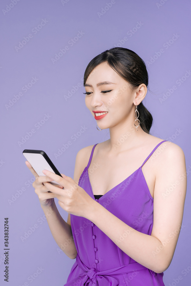 Smiling lovely young woman standing and using cell phone over violet background Smiling lovely young woman standing and using cell phone over violet background