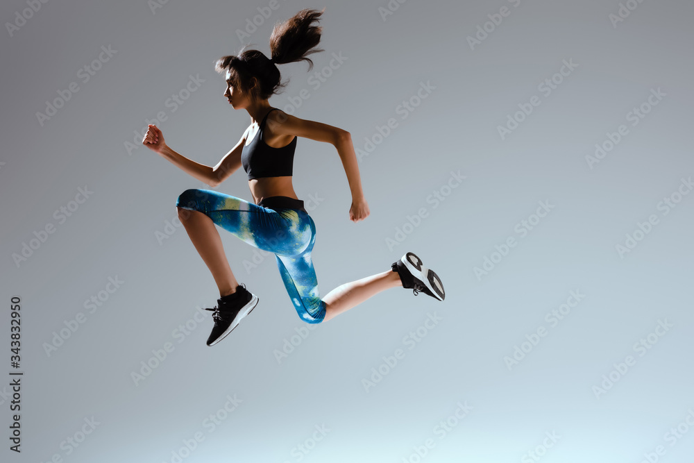 side view of african american girl in sportswear jumping on grey