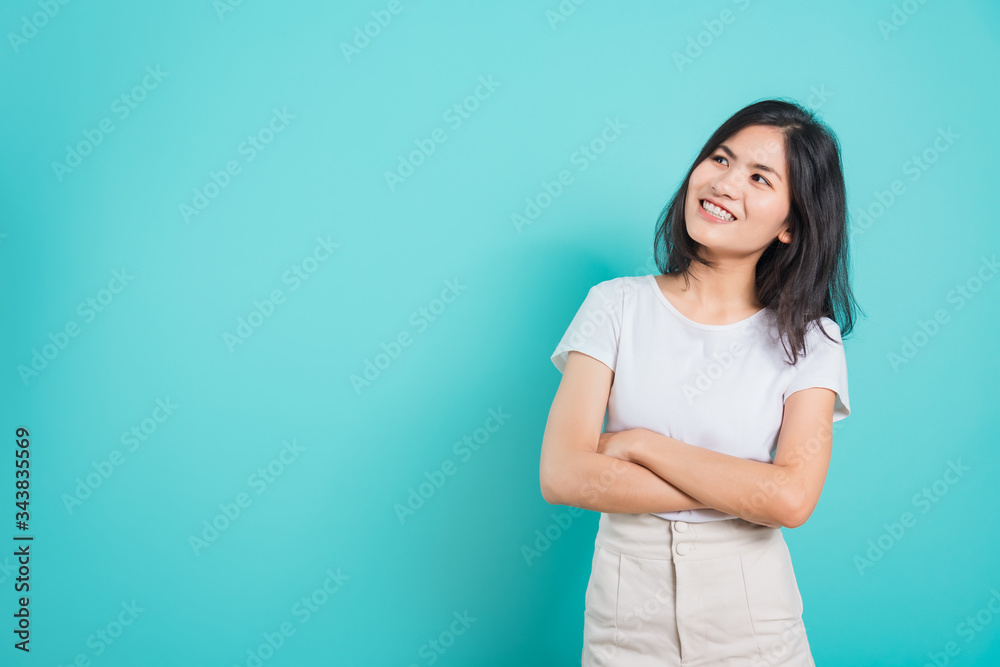 Portrait Asian beautiful happy young woman smile wear white t-shirt standing with a chest looking up away at copy space, on a blue background Portrait Asian beautiful happy young woman smile wear white t-shirt standing with a chest looking up away at copy space, on a blue background