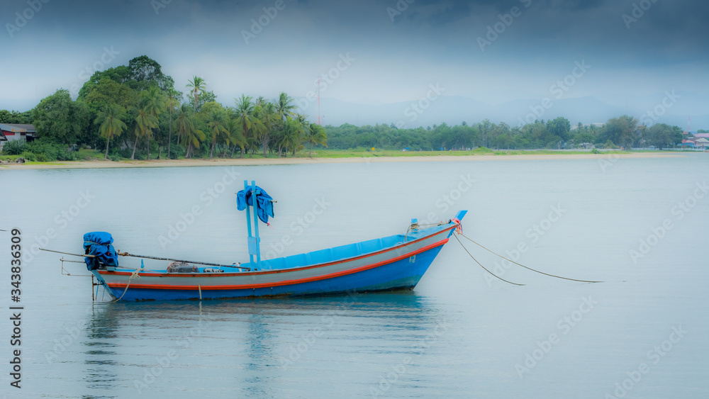 Blue traditional fishing boat at anchor with trees in the background and reflection in the water Blue traditional fishing boat at anchor with trees in the background and reflection in the water