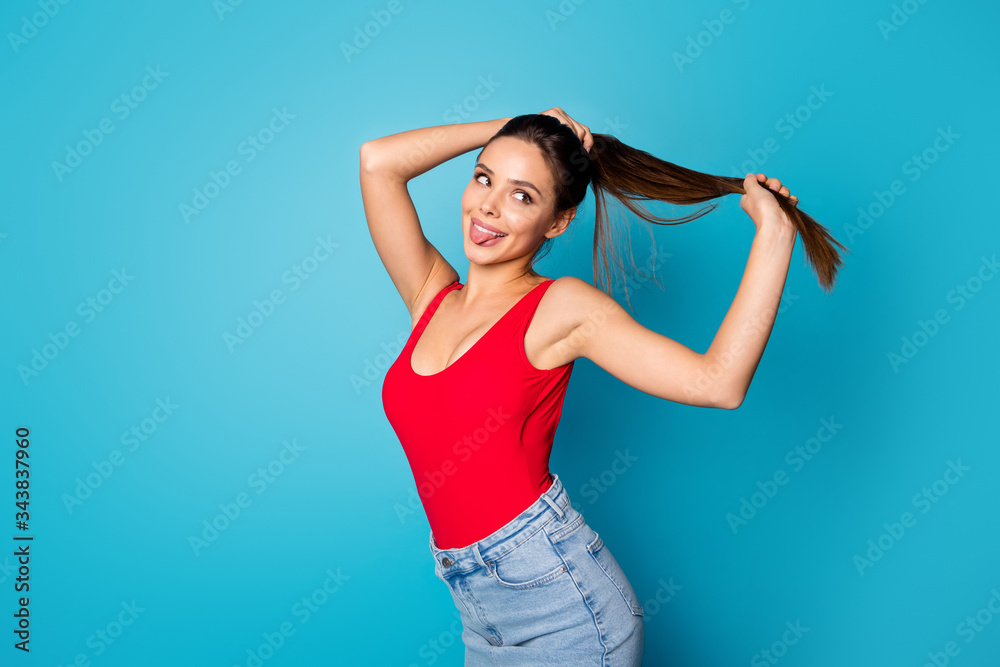 Portrait of cheerful sweet cute pretty youth girl hold hand ponytails enjoy spring anti dander silky haircare effect show tongue out wear red singlet denim isolated blue color background Portrait of cheerful sweet cute pretty youth girl hold hand ponytails enjoy spring anti dander silky haircare effect show tongue out wear red singlet denim isolated blue color background