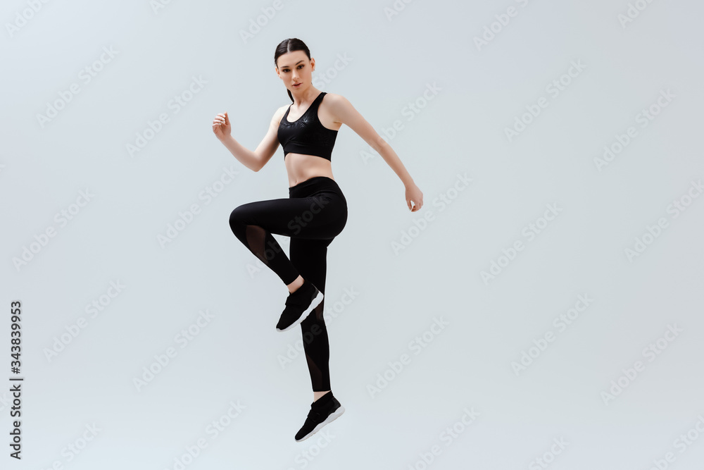 sportive woman in black sportswear jumping isolated on white
