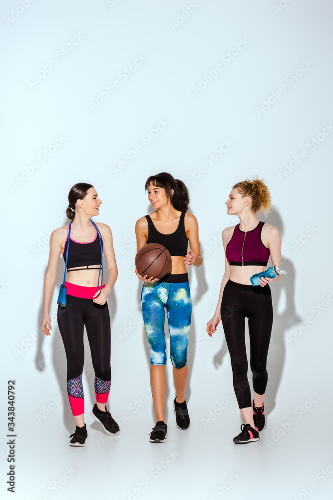 Fototapeta premium happy african american girl holding basketball and walking with sportive women on white