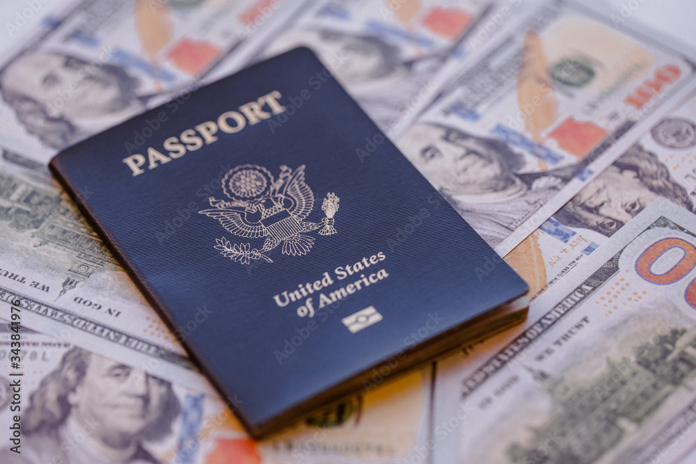 One single blue American passport on top of a pile of US dollars One single blue American passport on top of a pile of US dollars