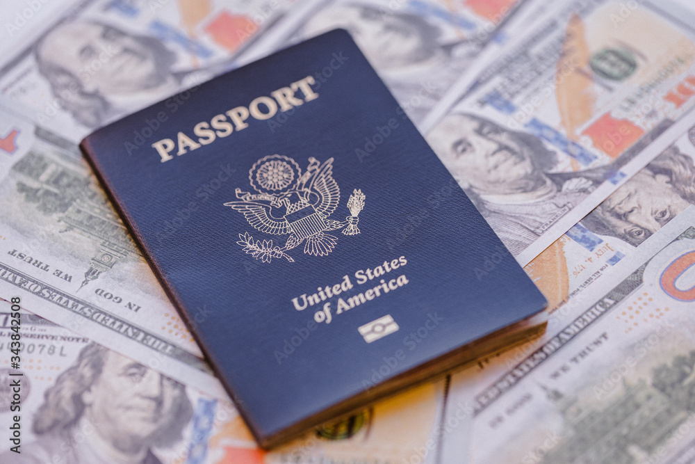 One single blue American passport on top of a pile of US dollars One single blue American passport on top of a pile of US dollars