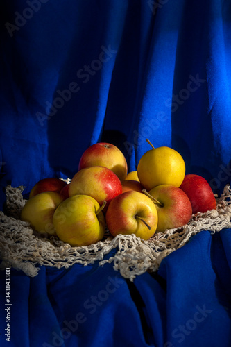 Spring still life with a group of scattered yellow-red apples on a blue background. Vertical orientation