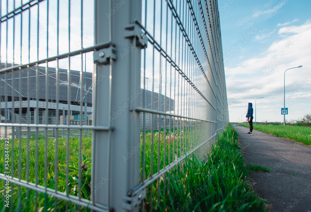 Obraz premium Sad Thoughtful teenage hipster girl standing alone in front of the metal grid