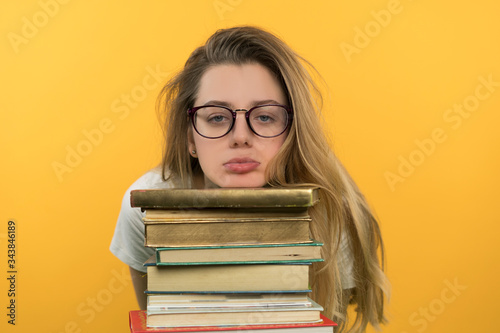 A young girl with glasses holds a pile of books, looks at them skeptically, does not want to study, a boring face