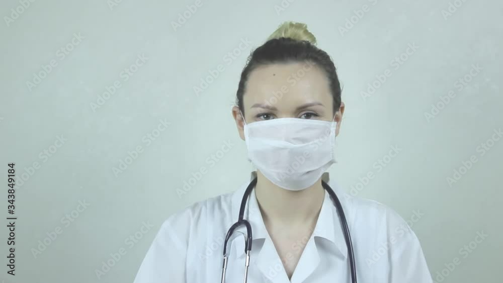 Young woman doctor in uniform, protective medical mask and medical gloves and with a stethoscope raises her hand with a clenched fist as a sign of readiness for resistance to diseases Young woman doctor in uniform, protective medical mask and medical gloves and with a stethoscope raises her hand with a clenched fist as a sign of readiness for resistance to diseases