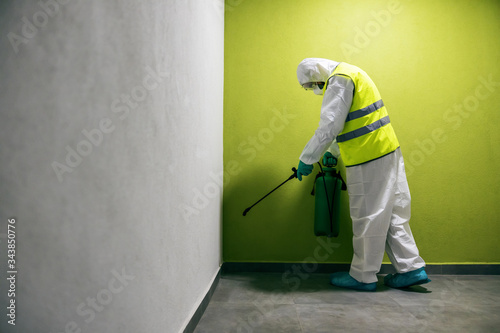 Full length of worker in sterile suit and vest sterilizing hall of a building from corona virus / covid 19.