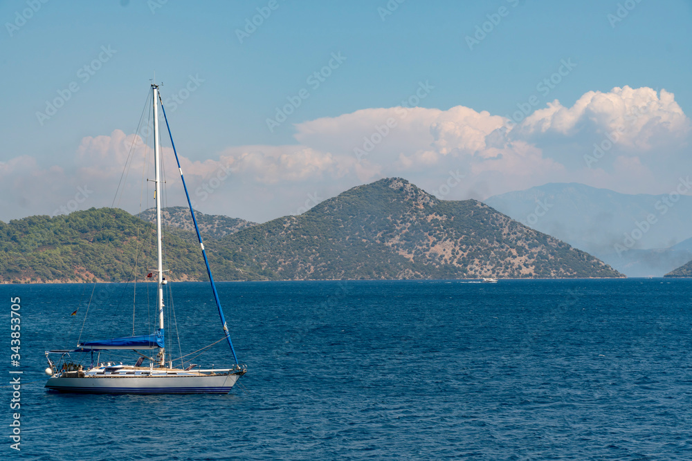 A single white sailing boat traveling in blue Aegean sea with mountain, sky and white clouds in background, with copy space.
A single white sailing boat traveling in blue Aegean sea with mountain, sky and white clouds in background, with copy space.