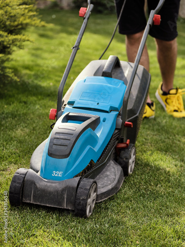 Young man mows grass with an electric lawn mower