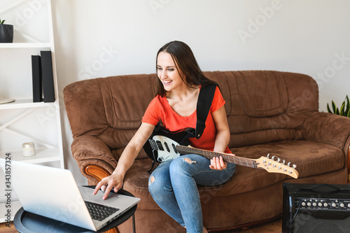 Online learning concept. Young woman watching video tutorials and learning to play the electric guitar, uses a combo amplifier photo