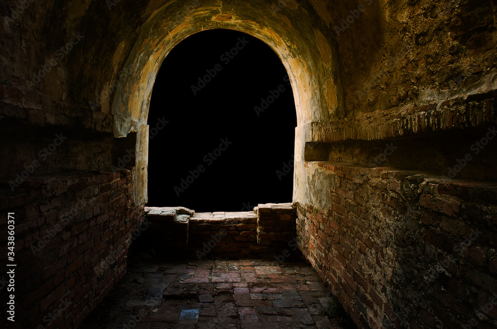 The ancient tunnel, aged construction of historical fortress isolated on black background; Dark in the tunnel, golden glow light or sunset at window.