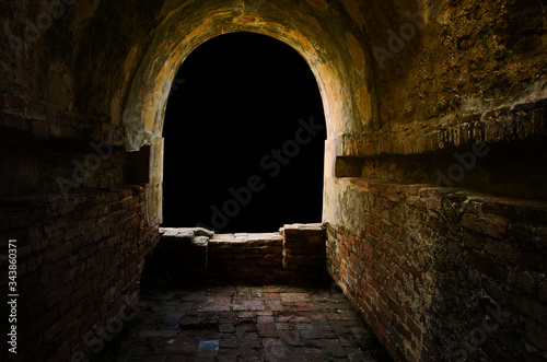 The ancient tunnel, aged construction of historical fortress isolated on black background; Dark in the tunnel, golden glow light or sunset at window.