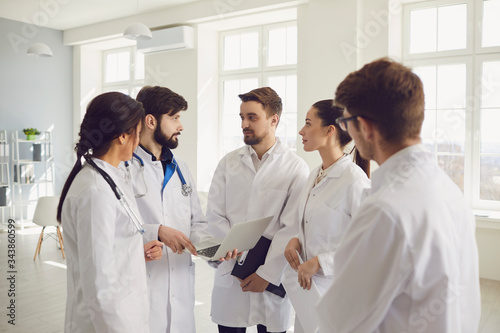Group of practicing doctors in a meeting discuss the diagnosis of a patient standing in a clinic office.